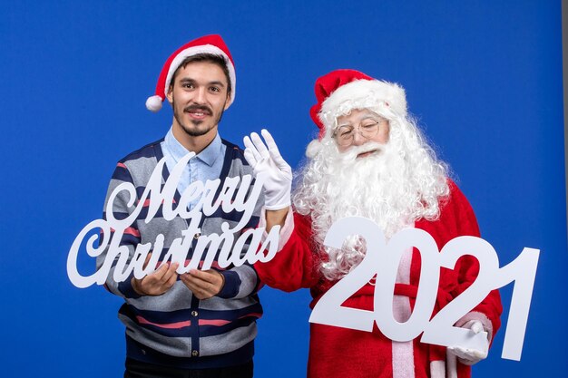 Vooraanzicht kerstman met jonge mannelijke holding en vrolijke kerstgeschriften op blauw
