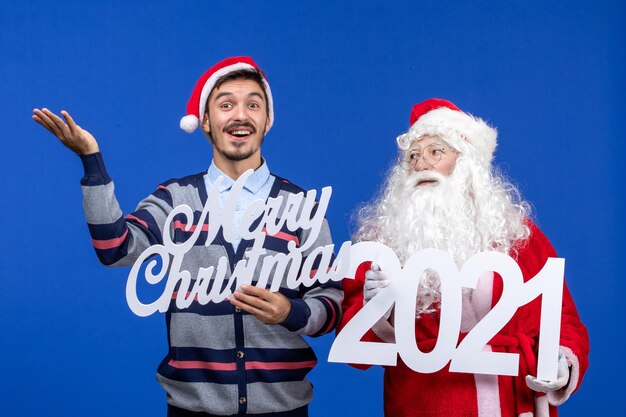 Vooraanzicht kerstman met jonge mannelijke holding en vrolijke kerstgeschriften op blauwe kerstkleur