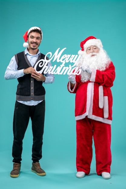 Vooraanzicht kerstman met jonge mannelijke whos die vrolijke kerstmis houden die op blauwe achtergrond schrijven