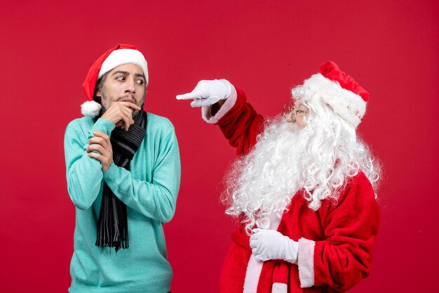 Vooraanzicht kerstman met man die gewoon op de rode huidige vakantie kerstemotie staat