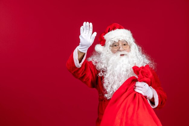 Vooraanzicht kerstman met rode tas vol cadeautjes groet op rode kerst