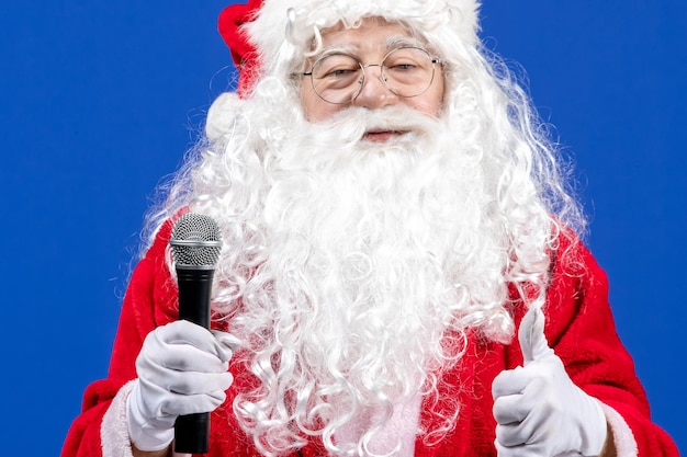 Vooraanzicht kerstman met rood pak en witte baard met microfoon op de blauwe kleur vakantie xmas nieuwjaarssneeuw