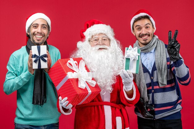 Vooraanzicht kerstman met twee mannen die cadeautjes vasthouden op de rode emotie rode nieuwjaarscadeau xmas
