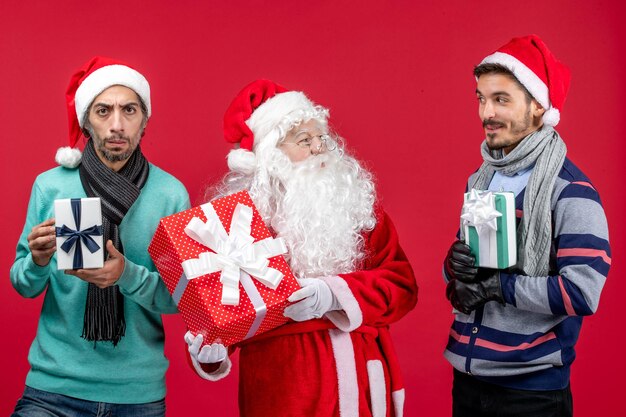 Vooraanzicht kerstman met twee mannen die cadeautjes vasthouden op rode cadeau-emotie kerstmis nieuwjaar rood