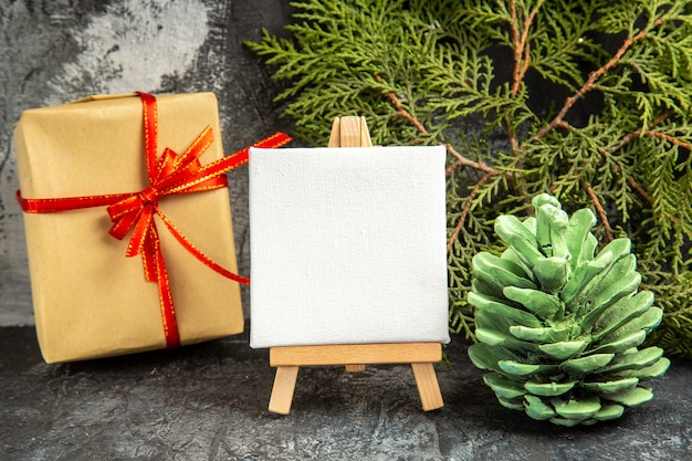 Vooraanzicht klein geschenk gebonden met rood lint mini canvas op houten ezel dennentak op grijs