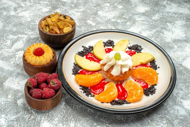 Vooraanzicht kleine cake met gesneden fruit en rozijnen op een witte achtergrond, zoet fruitkoekje, suikerkoekjescake