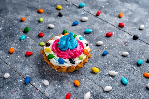 Vooraanzicht kleine lekkere cake met room en verschillende kleurrijke snoepjes allemaal op licht