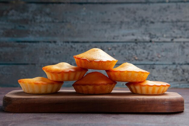 Vooraanzicht kleine lekkere taarten die op elkaar zijn gevoerd op de donkere achtergrond, zoete taartkoekjeskoekjestheecake