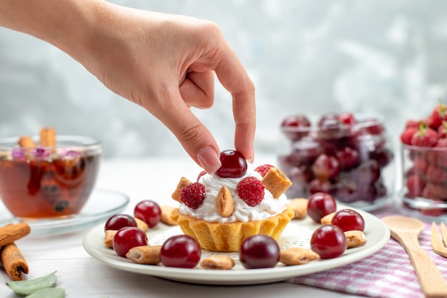 Vooraanzicht kleine romige cake met frambozen, kersen en kleine koekjes die door vrouwtje op licht bureau nemen