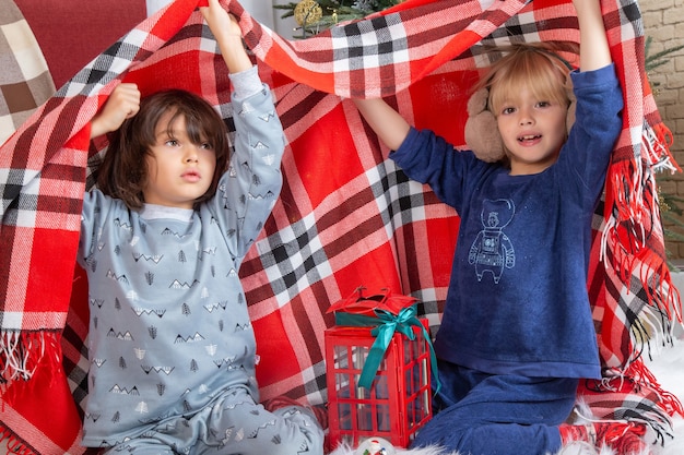 Vooraanzicht kleine schattige jongens die zich verstoppen met een laken rond de kerstboom