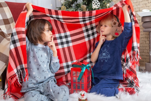 Vooraanzicht kleine schattige jongens die zich verstoppen met een laken rond de kerstboom