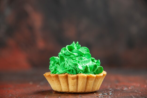 Vooraanzicht kleine taart met groene banketbakkersroom op donkerrode tafel met kopieerruimte