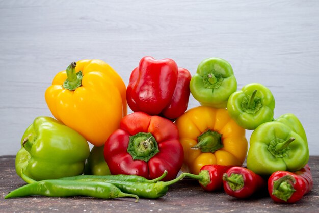 Vooraanzicht kleurrijke paprika's met paprika's op de bruine groentekleur op het bureau