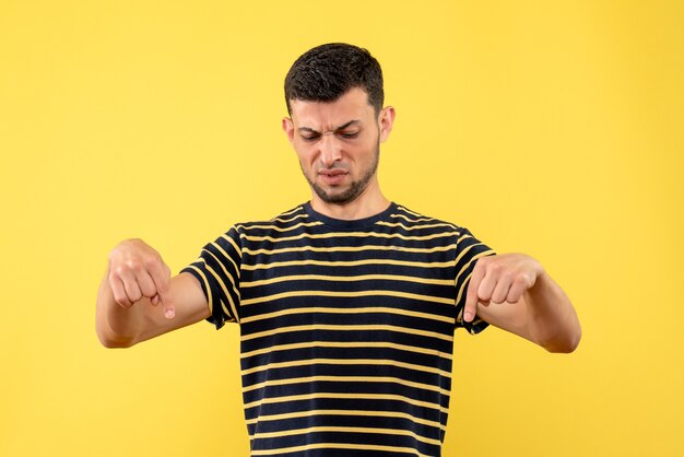 Vooraanzicht knappe man in zwart-wit gestreept t-shirt wijzend op vloer gele geïsoleerde achtergrond