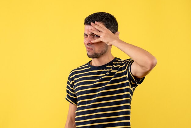 Vooraanzicht knipperde - ogen jonge man in zwart-wit gestreept t-shirt op gele geïsoleerde achtergrond