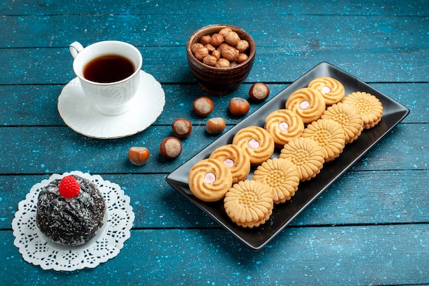 Vooraanzicht kopje thee met noten en koekjes op de rustieke blauwe cake van het het koekje van de bureausuiker