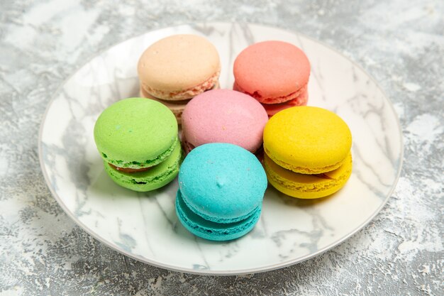 Vooraanzicht lekkere Franse macarons kleurrijke taarten binnen plaat op witte oppervlakte cake suiker koekje zoete taartkoekjes