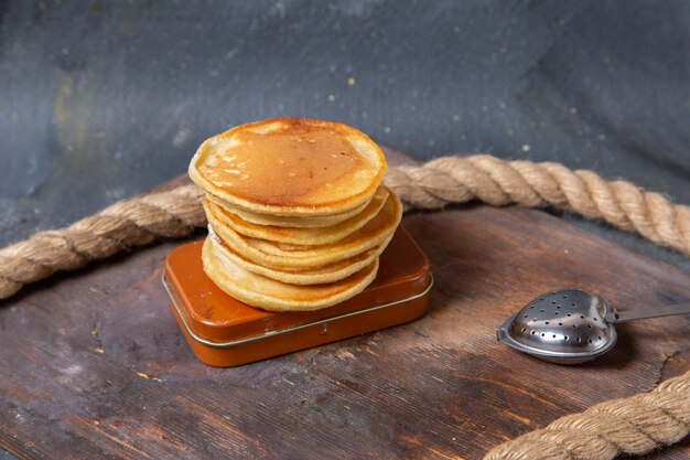 Vooraanzicht lekkere heerlijke pannenkoeken op het houten bureau met touwen op de grijze achtergrond voedsel maaltijd ontbijt zoete muffin