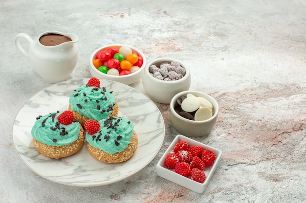 Vooraanzicht lekkere kleine taarten met kleurrijke snoepjes en koekjes op witte achtergrond dessert taart taart regenboog kleur snoep