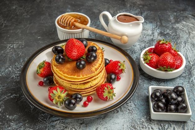 Vooraanzicht lekkere pannenkoeken met honing en fruit op lichte cake van het oppervlakte zoete fruit