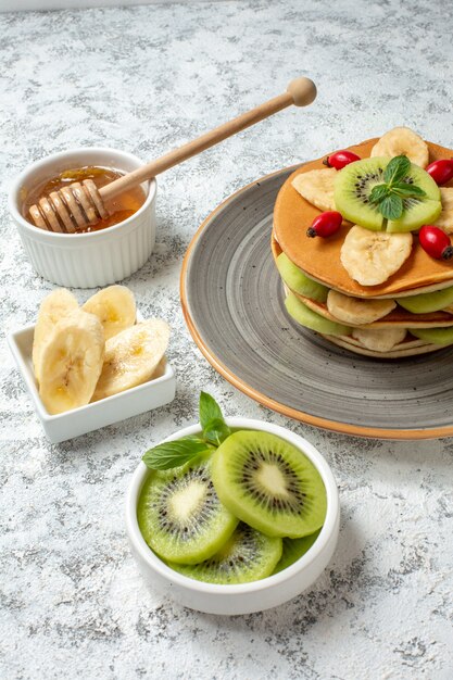 Vooraanzicht lekkere pannenkoeken met honing en gesneden fruit op het witte oppervlak