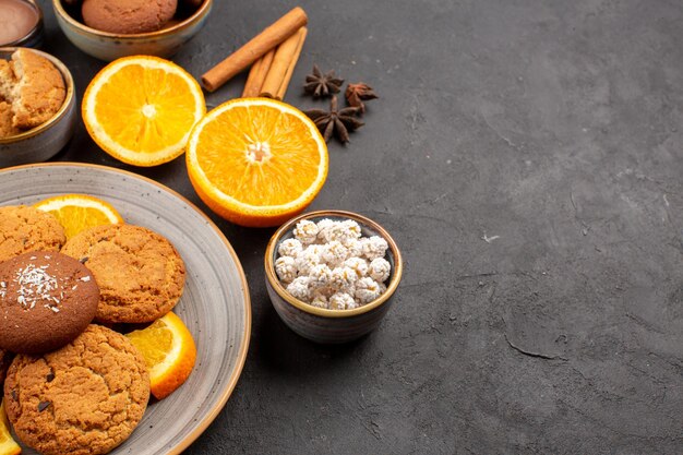 Vooraanzicht lekkere zandkoekjes met vers gesneden sinaasappels op een donkere achtergrond, fruitkoekje, zoete koekje, citrussuiker