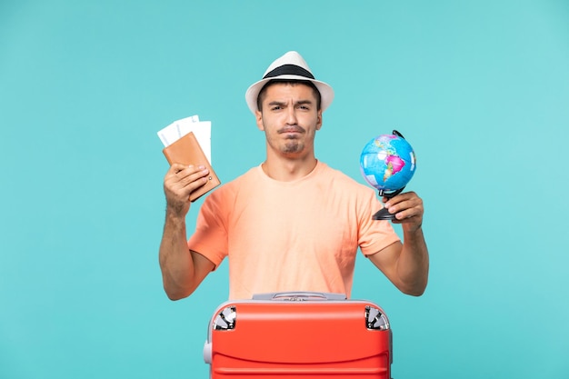 Gratis foto vooraanzicht man in vakantie met kleine wereldbol en kaartjes op lichtblauw