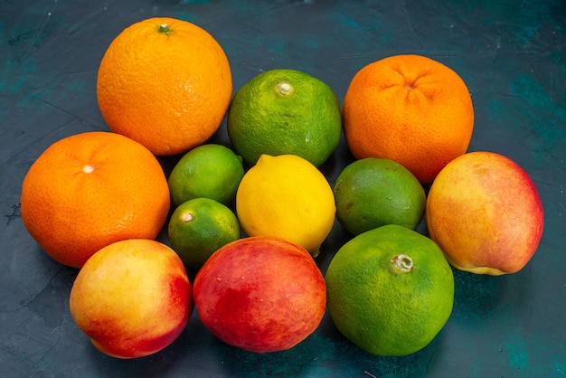 Gratis foto vooraanzicht mandarijnen en perziken vers zacht fruit op donkerblauw bureau fruit vitamine exotische citrus