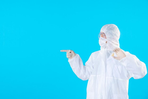 Vooraanzicht mannelijke arts in beschermend pak en masker met een kleine fles op blauw