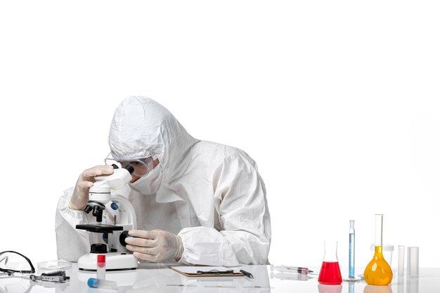 Vooraanzicht mannelijke arts in beschermend pak en met masker met behulp van microscoop op witte ruimte