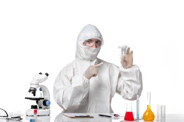 Vooraanzicht mannelijke arts in beschermend pak lege kolf op lichte witte ruimte te houden