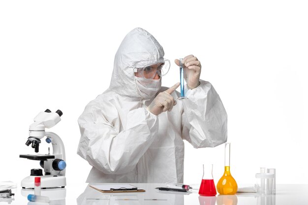 Vooraanzicht mannelijke arts in beschermend pak met masker vanwege covid bedrijf kolf met blauwe oplossing op witte ruimte