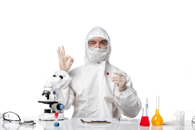 Vooraanzicht mannelijke arts in beschermend pak met masker vanwege covid bedrijf kolf op witte ruimte
