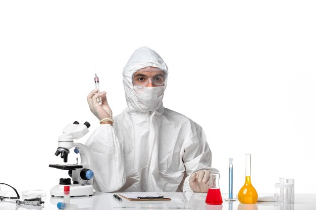 Vooraanzicht mannelijke arts in beschermend pak met masker vanwege covid-injectie op witte ruimte