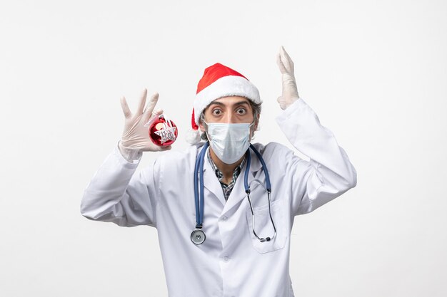 Vooraanzicht mannelijke arts in masker met stuk speelgoed op het witte virus van het muurgezondheid covid nieuwe jaar
