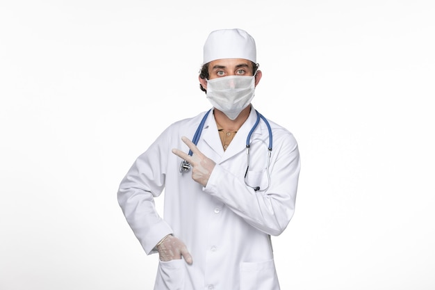 Vooraanzicht mannelijke arts in medisch pak draagt zijn masker tegen coronavirus op wit bureau coronavirus virus pandemische geneeskunde