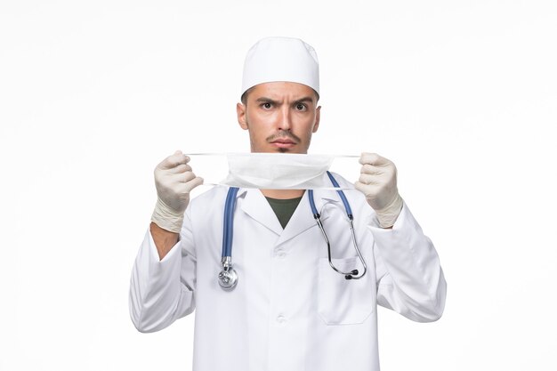Vooraanzicht mannelijke arts in medisch pak en draagt een masker tegen coronavirus op witte muur virus covid - ziekte ziekte pandemie