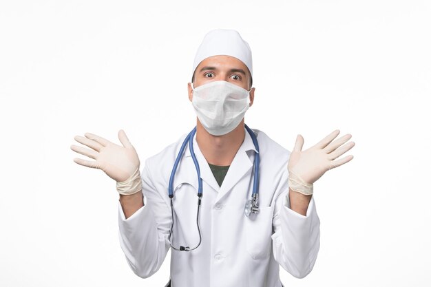Vooraanzicht mannelijke arts in medisch pak en draagt masker vanwege covid- op witte vloer covid-virus geneeskunde pandemische ziekte