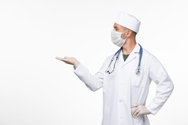 Vooraanzicht mannelijke arts in medisch pak en het dragen van een masker tegen covid met stethoscoop op witte muur virus covid- ziekte ziekte pandemie