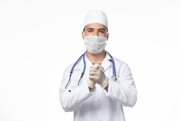 Vooraanzicht mannelijke arts in medisch pak en het dragen van een masker tegen covid op de lichte witte muur covid virus ziekte geneeskunde pandemie
