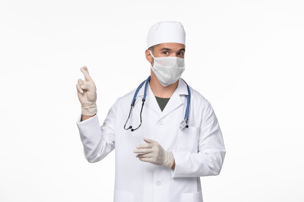 Vooraanzicht mannelijke arts in medisch pak en het dragen van een masker tegen covid op lichte witte muur virus covid- ziekte ziekte pandemie
