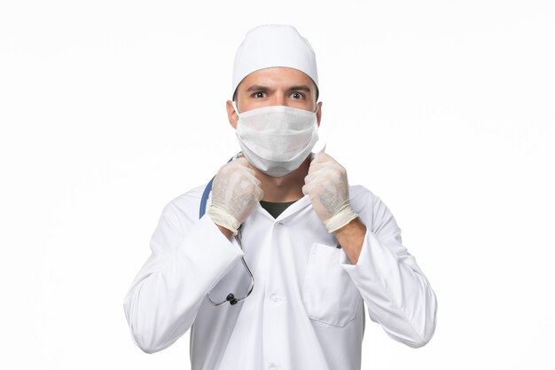 Vooraanzicht mannelijke arts in medisch pak en masker dragen vanwege covid-on white wall-ziekte virus covid-pandemische ziekte