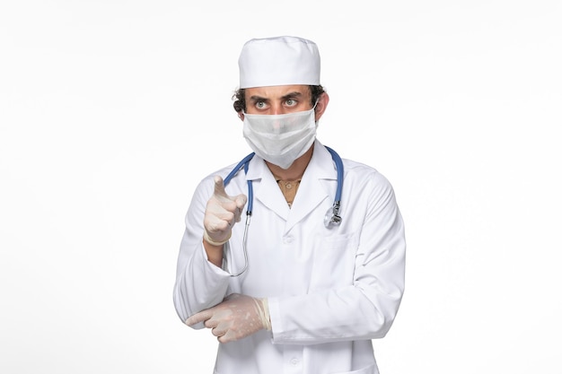 Vooraanzicht mannelijke arts in medisch pak met masker als bescherming tegen covid - op lichte witte muur virusplons coronavirus pandemie