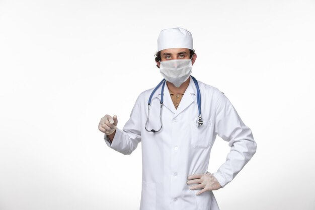 Vooraanzicht mannelijke arts in medisch pak met masker als bescherming tegen covid- op witte muur virusziekte covid- pandemie
