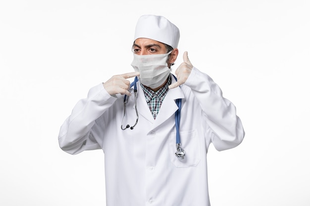 Vooraanzicht mannelijke arts in medisch pak met masker vanwege covid op wit oppervlak