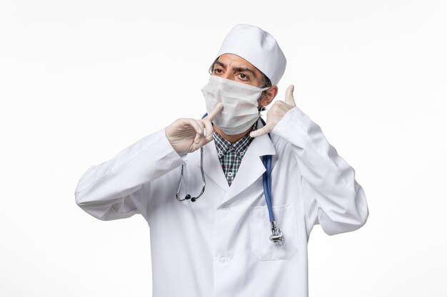 Vooraanzicht mannelijke arts in medisch pak met masker vanwege covid - op witte vloer ziekte virus covid - ziekenhuis pandemie