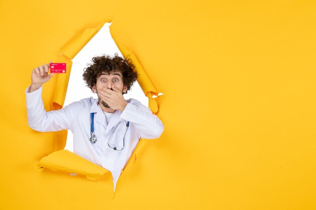 Vooraanzicht mannelijke arts in medisch pak met rode bankkaart op gele geneeskunde ziekenhuisziekte virus medic geld gezondheid