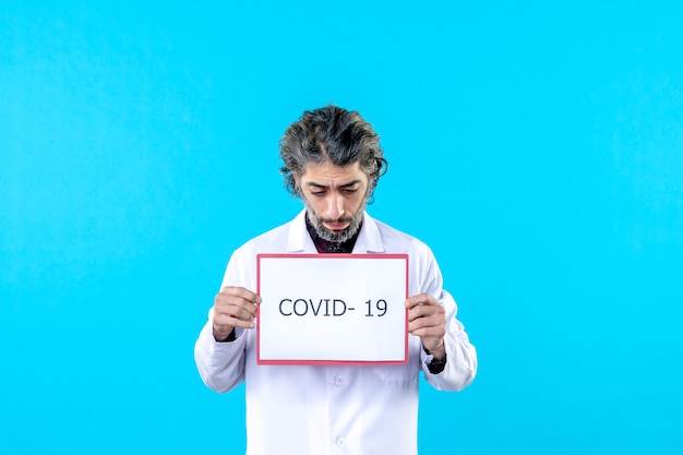 Vooraanzicht mannelijke arts in medisch uniform met covid-schrijven op het blauw