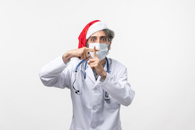 Vooraanzicht mannelijke arts in steriel masker op witte muurvirus covid nieuwjaarsvakantie