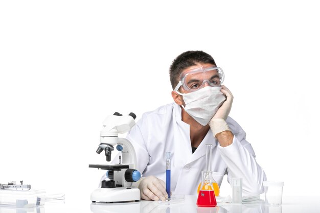 Vooraanzicht mannelijke arts in wit medisch pak met masker vanwege covid werken en benadrukt op witte ruimte